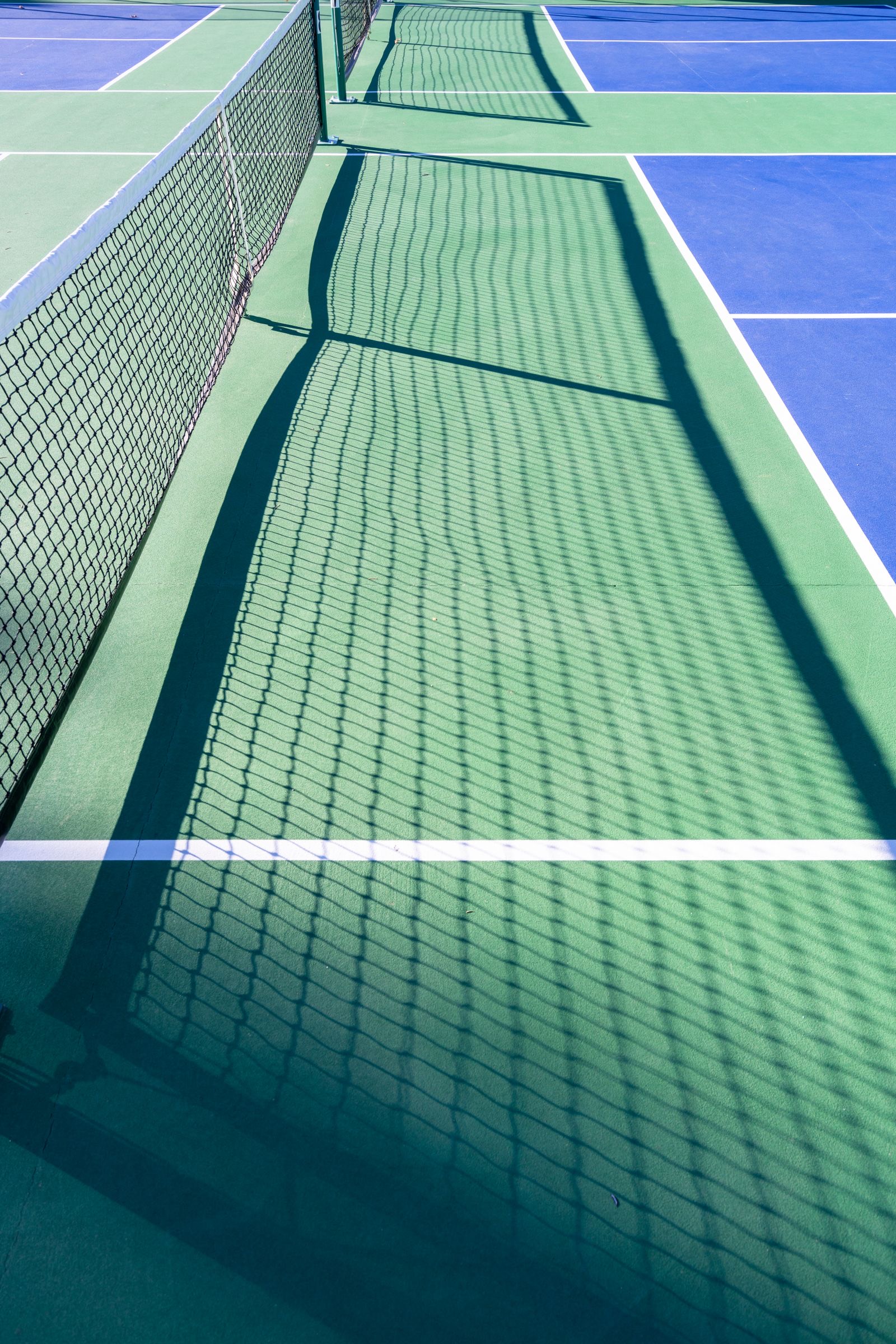 Net shadow across a freshly cleaned blue and green pickleball court